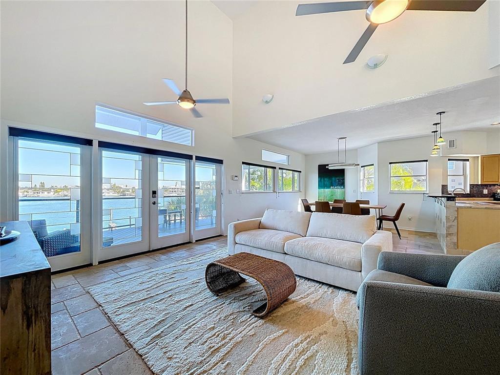 A living room with vaulted ceilings, tile floors, and sliding glass doors overlooking the water — 8485 BLIND PASS DRIVE, TREASURE ISLAND, FL