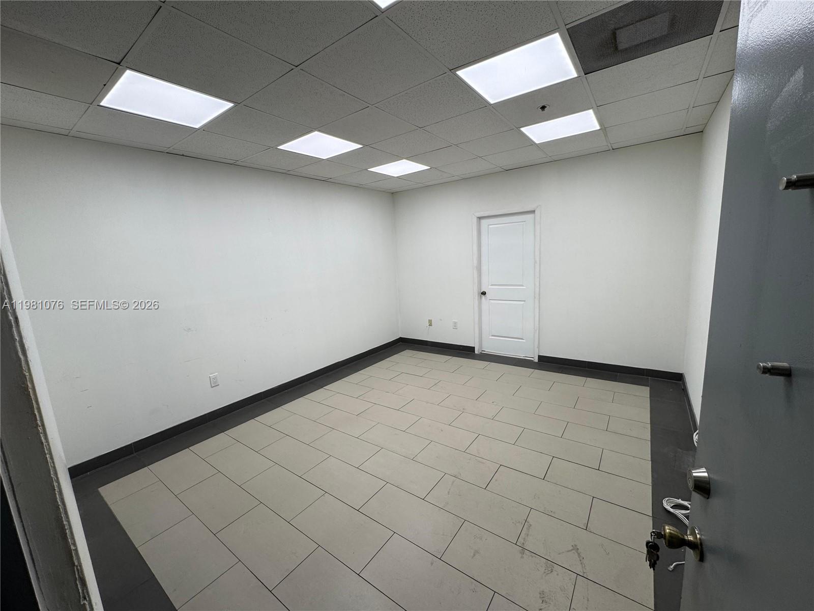 An empty office room features white walls, a drop ceiling, and light-colored tiled flooring — 900 W 49th St Suite 538, Hialeah FL 33012, HIALEAH, FL