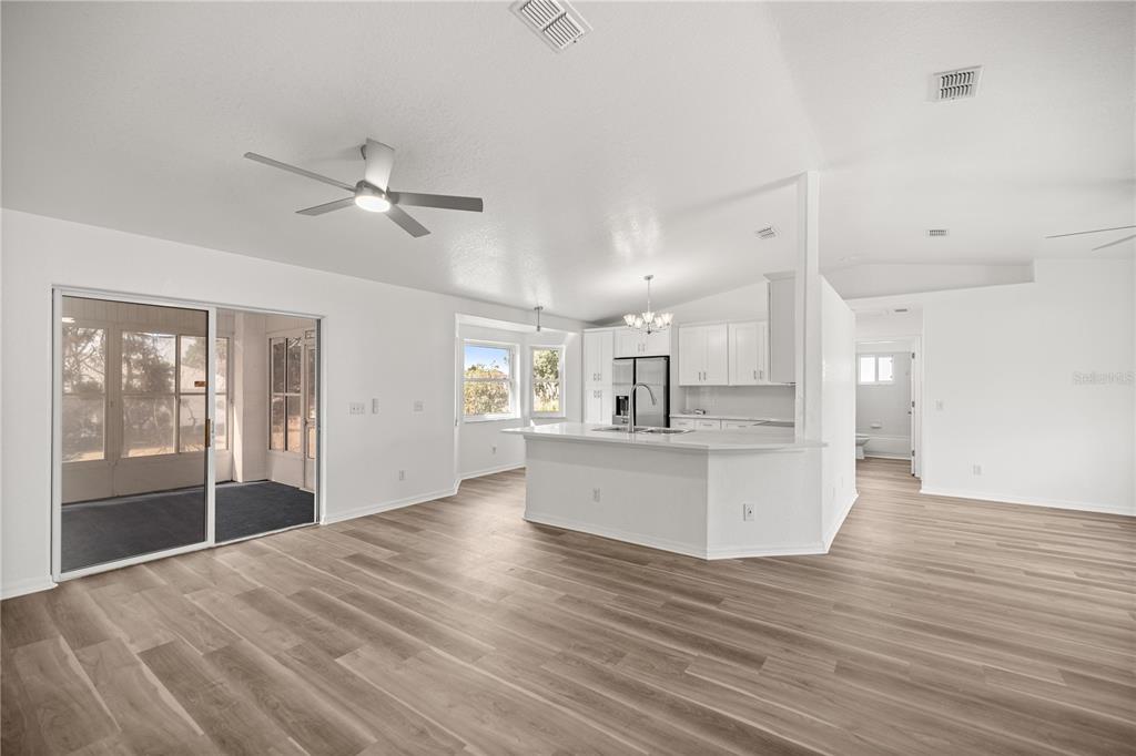 An open-concept kitchen and living area featuring white cabinetry, a central island, and wood-look flooring — 9920 SW 63RD COURT, OCALA, FL