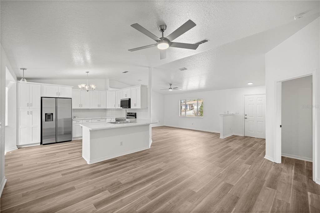 A bright open-concept kitchen and living area with white cabinetry and light wood-look flooring — 9920 SW 63RD COURT, OCALA, FL