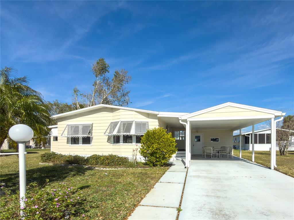 A single-story mobile home with light yellow siding, a carport, and a concrete driveway — 47 QUAIL COURT, ELLENTON, FL