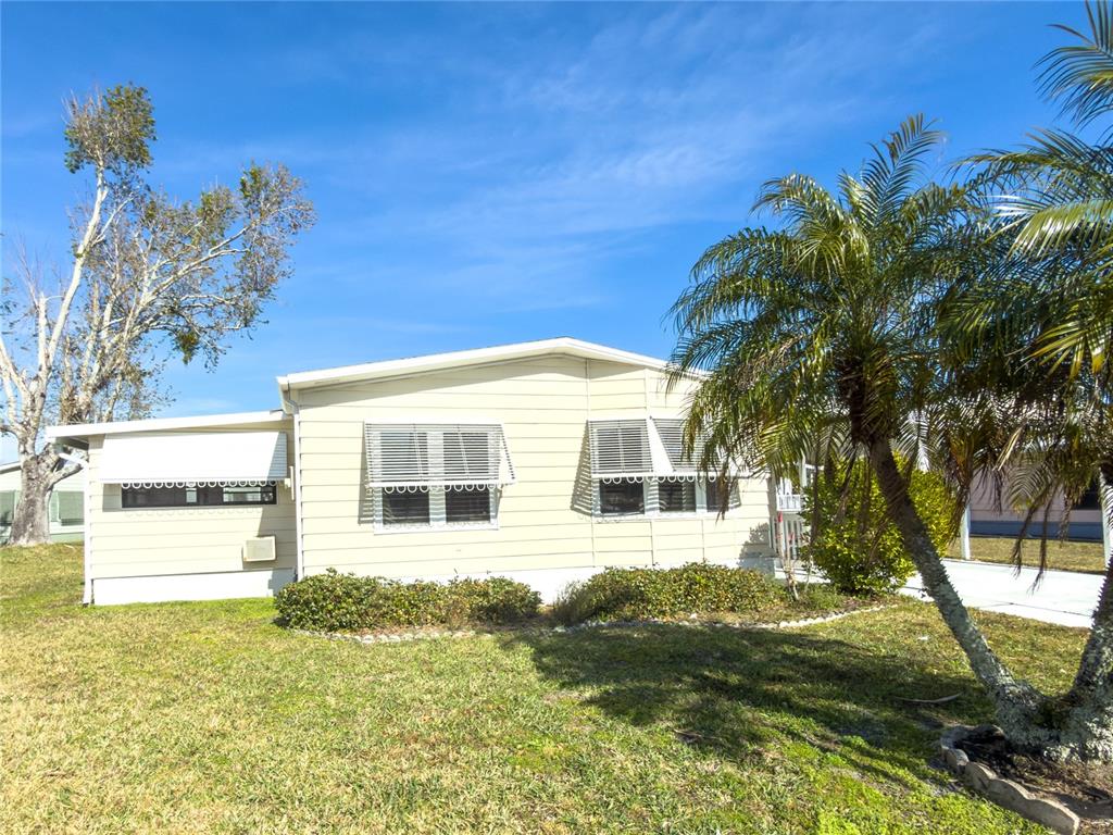 A single-story manufactured home with light siding, white trim, and a palm tree in front — 47 QUAIL COURT, ELLENTON, FL