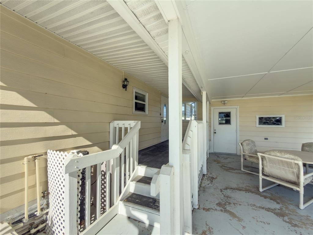 A covered porch with stairs, white railings, and outdoor furniture leads to a house entrance — 47 QUAIL COURT, ELLENTON, FL
