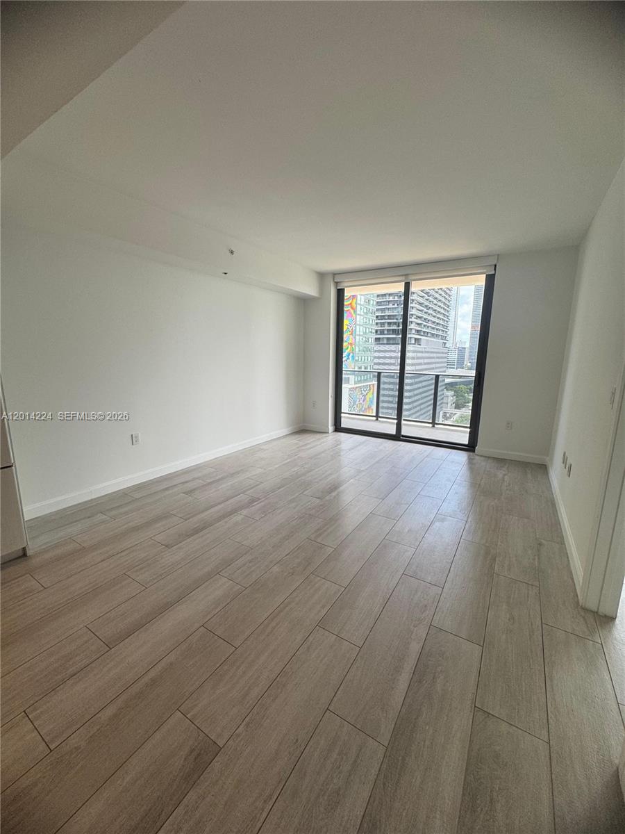 An empty room features light wood-look tile flooring, white walls, and a glass balcony door — 45 SW 9th St # 1104, Miami FL 33130, MIAMI, FL