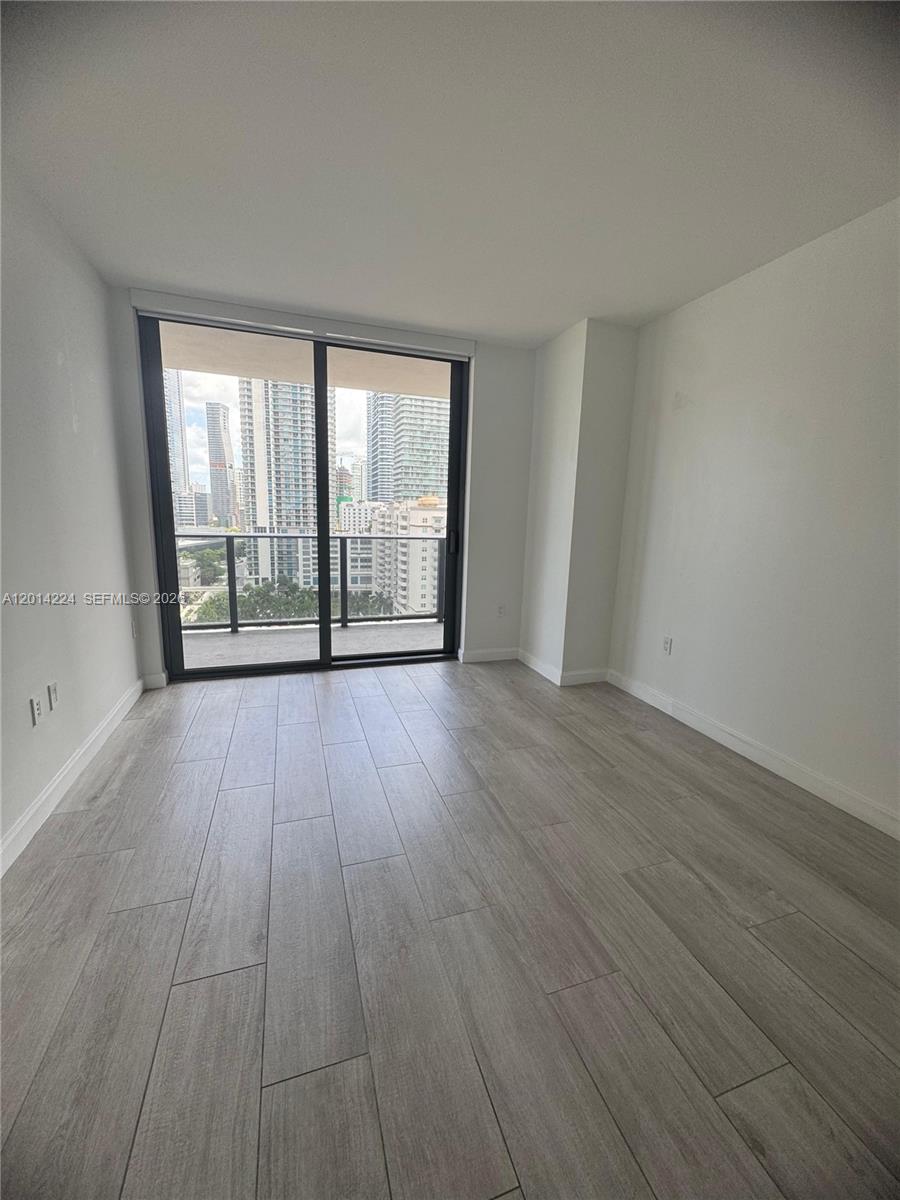 An empty room with light wood-look tile flooring and a sliding glass door to a balcony — 45 SW 9th St # 1104, Miami FL 33130, MIAMI, FL