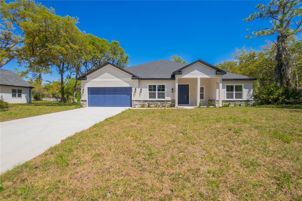 A single-story house with a blue garage door, light-colored siding, and a stone-accented front — 9695 E BAYMEADOWS DRIVE, INVERNESS, FL