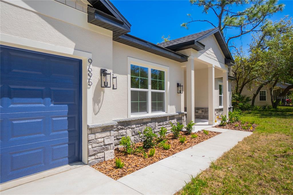 A single-story house exterior features a blue garage door, stone veneer, and a covered porch — 9695 E BAYMEADOWS DRIVE, INVERNESS, FL