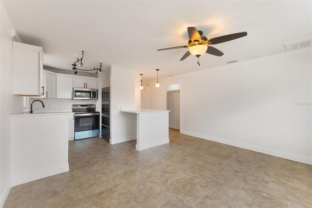 A kitchen with white cabinets and stainless steel appliances opens to a tiled living area — 14036 MARGUERITE DRIVE, MADEIRA BEACH, FL