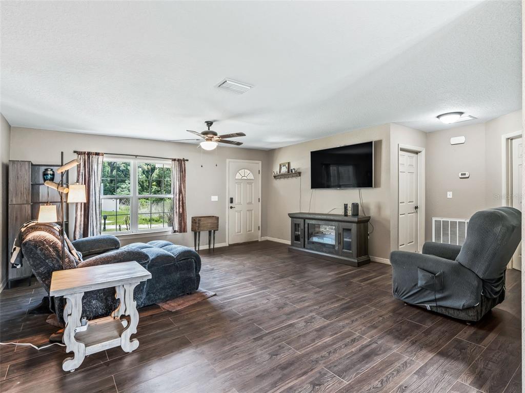 A living room features dark wood-look tile flooring, a ceiling fan, and a wall-mounted television — 4243 SE 131ST LANE, BELLEVIEW, FL