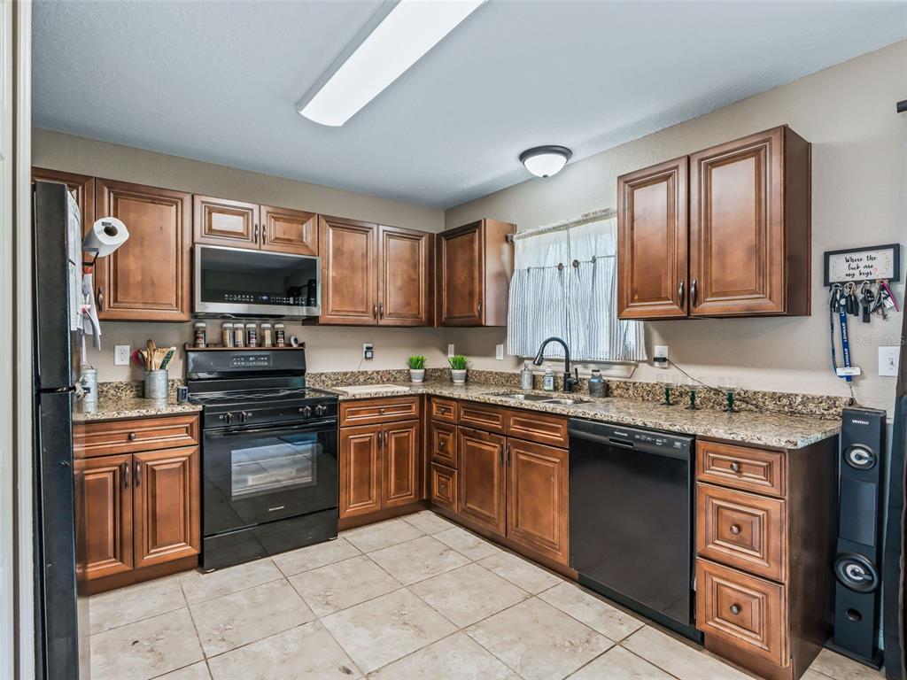 A kitchen with wood cabinets, granite countertops, black appliances, and light-colored tile flooring — 4243 SE 131ST LANE, BELLEVIEW, FL
