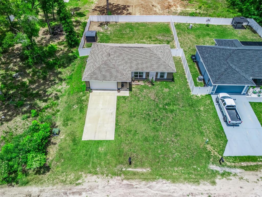 An aerial view shows a single-story house with a concrete driveway and a fenced backyard — 4243 SE 131ST LANE, BELLEVIEW, FL