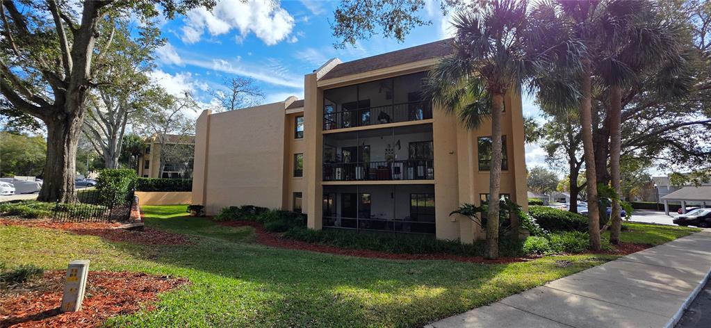 A three-story tan apartment building features screened balconies and is surrounded by trees and landscaping — 630 CRANES WAY UNIT 203, ALTAMONTE SPRINGS, FL
