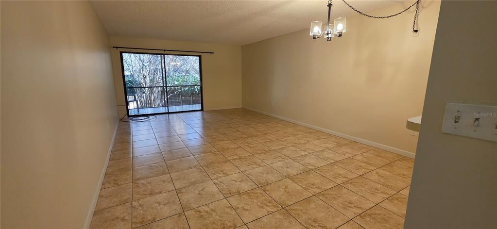 An empty room with beige tile flooring, light-colored walls, a chandelier, and a sliding glass door — 630 CRANES WAY UNIT 203, ALTAMONTE SPRINGS, FL