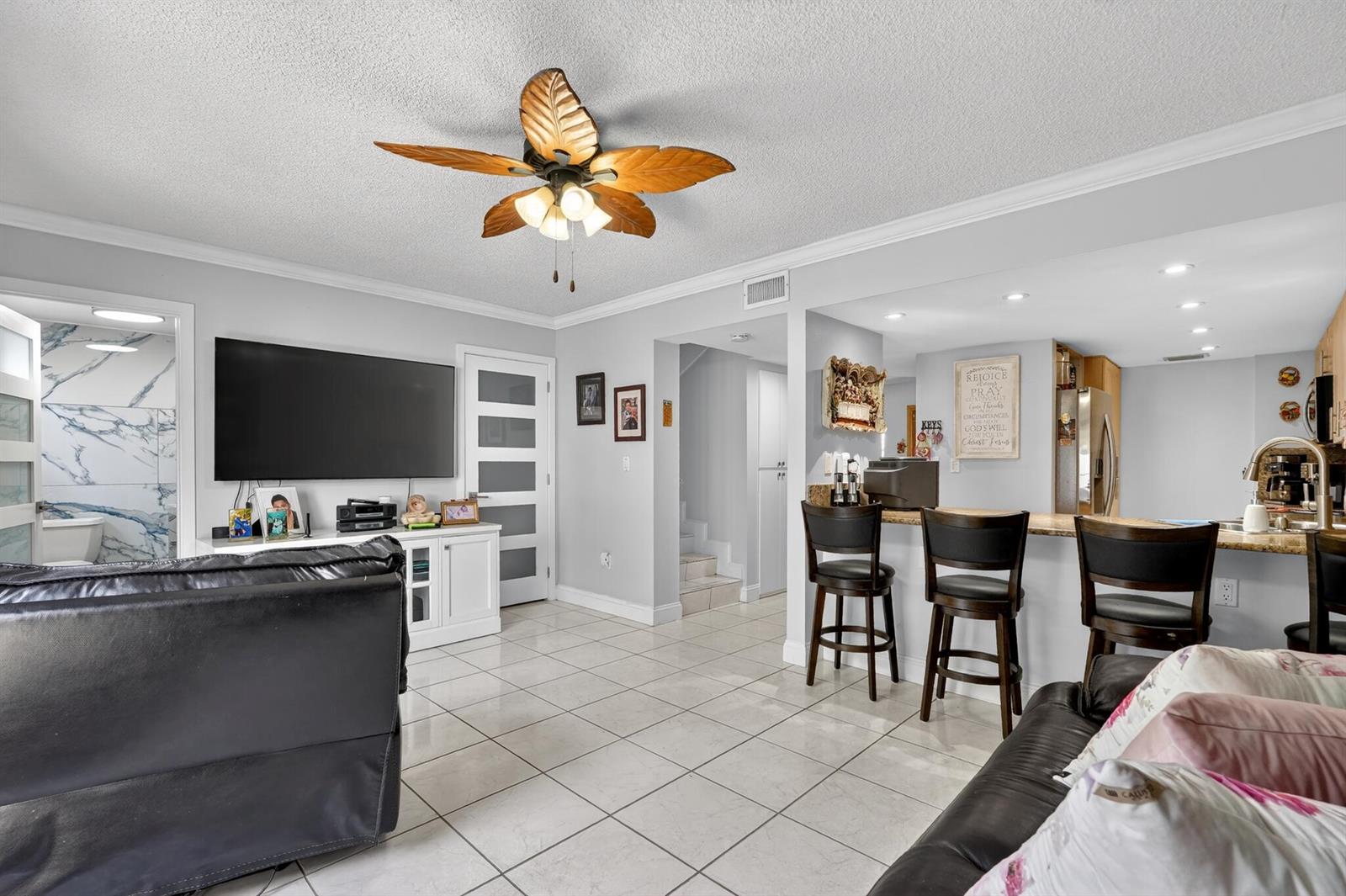 A living room with tile floors, a ceiling fan, a television, and a kitchen breakfast bar — 7101 W 24th Avenue # 45, Hialeah FL 33016, HIALEAH, FL
