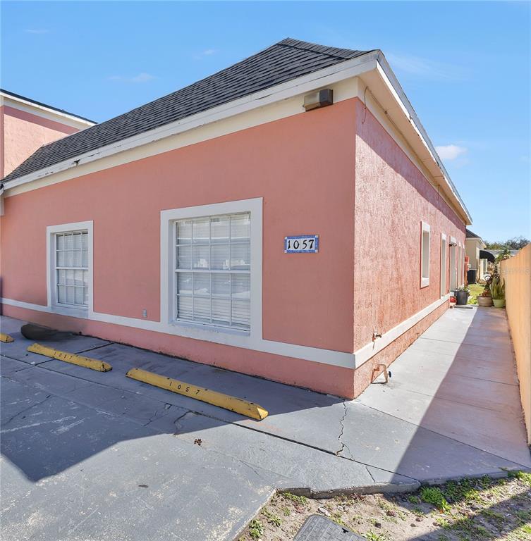 The exterior of a peach-colored building features white trim, two windows, and numbered parking stops — 1057 UNIVERSAL REST PLACE, KISSIMMEE, FL