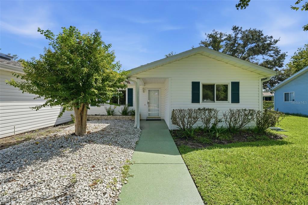 A white single-story house with a green walkway, a tree, and a gravel front yard — 17989 SE 106TH COURT, SUMMERFIELD, FL