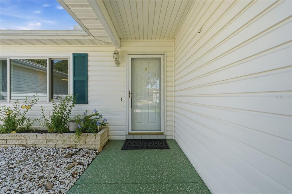 A white house exterior features a front door, a green porch, and a stone planter — 17989 SE 106TH COURT, SUMMERFIELD, FL