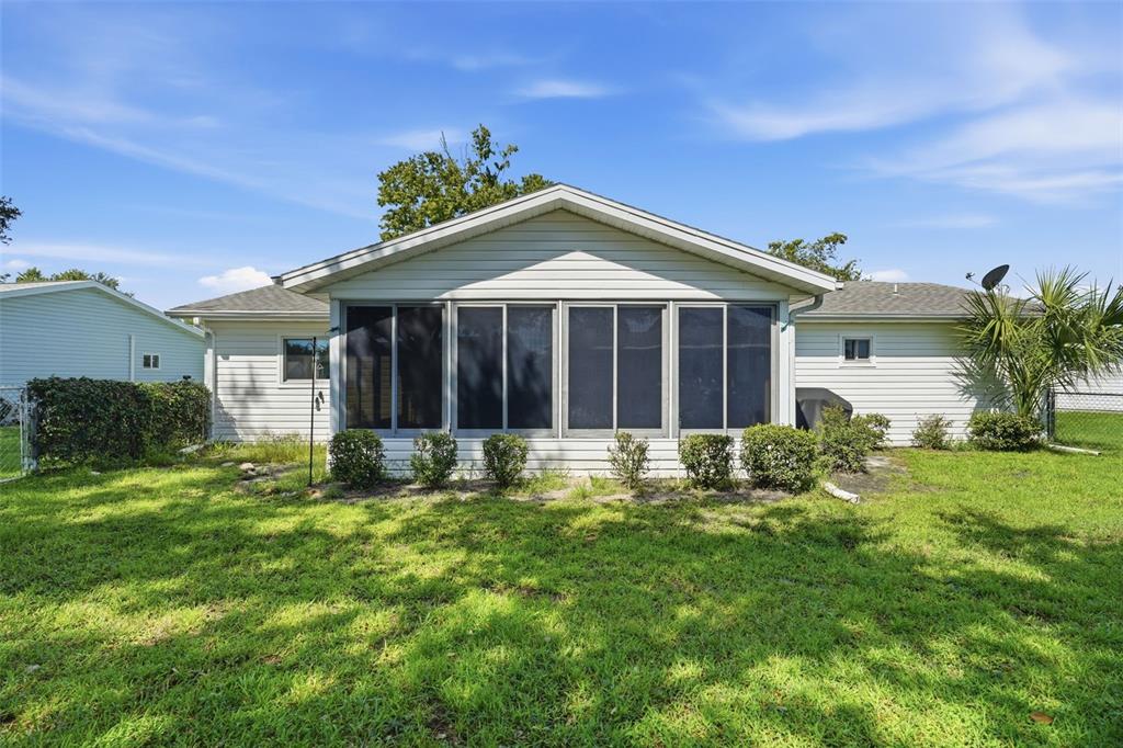 The back exterior of a single-story house features a screened-in porch and a grassy yard — 17989 SE 106TH COURT, SUMMERFIELD, FL