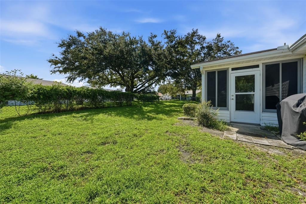 A grassy backyard features a chain-link fence, large shade trees, and a screened-in porch — 17989 SE 106TH COURT, SUMMERFIELD, FL