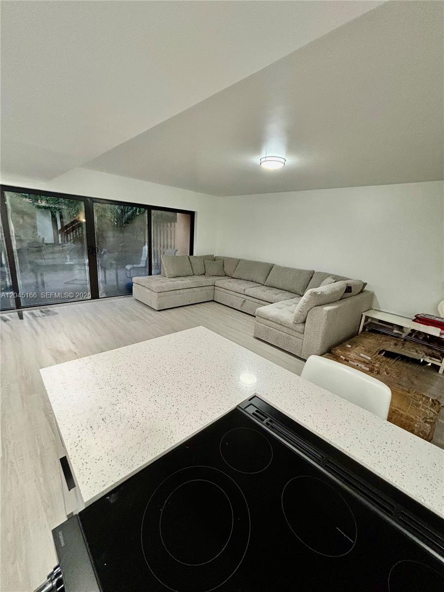 A kitchen island with a black cooktop overlooks a living room featuring a large sectional — 8010 NW 27th Pl # 8010, Sunrise FL 33322, SUNRISE, FL