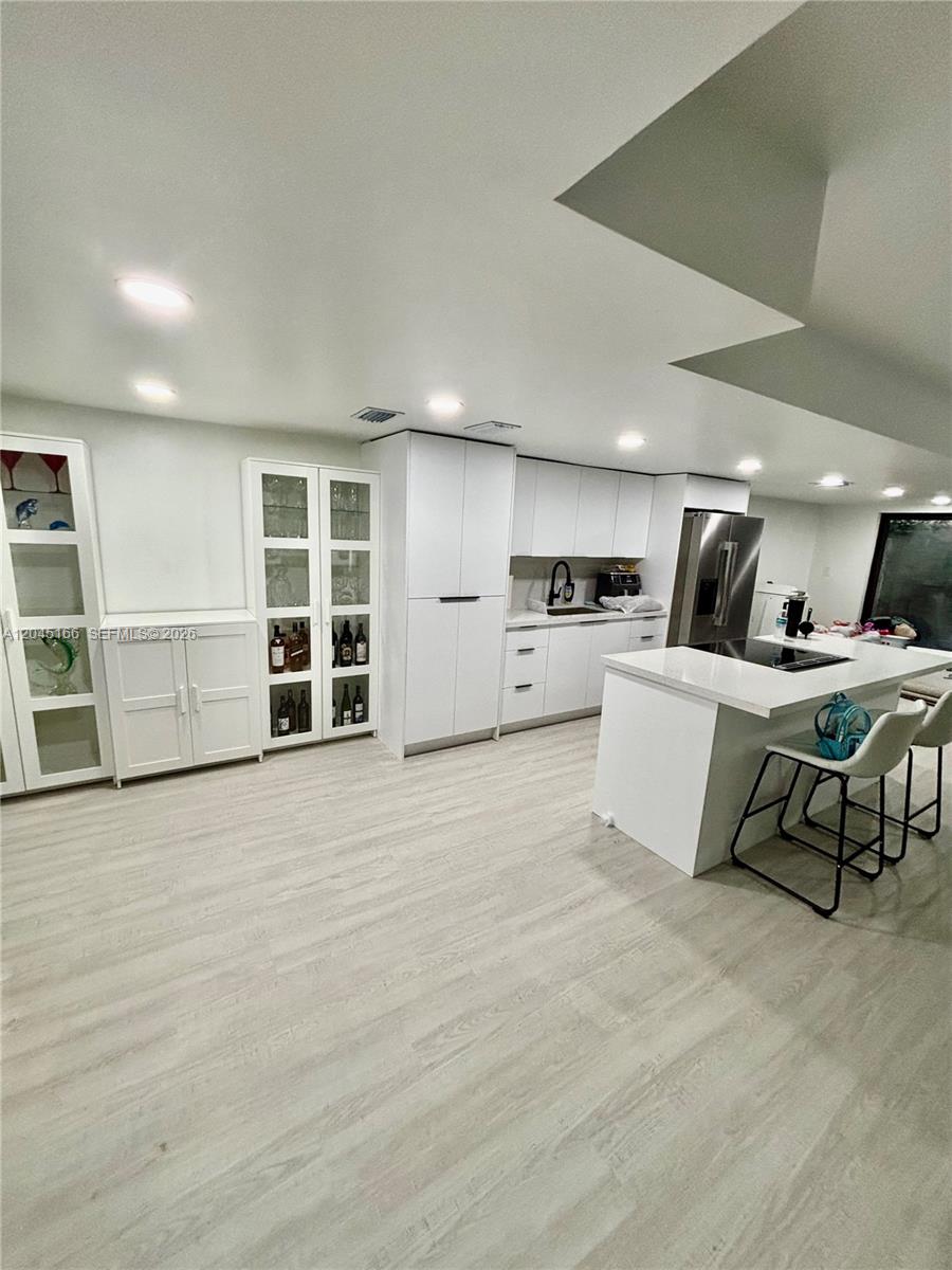 A modern kitchen features white cabinetry, a central island with seating, and light wood flooring — 8010 NW 27th Pl # 8010, Sunrise FL 33322, SUNRISE, FL