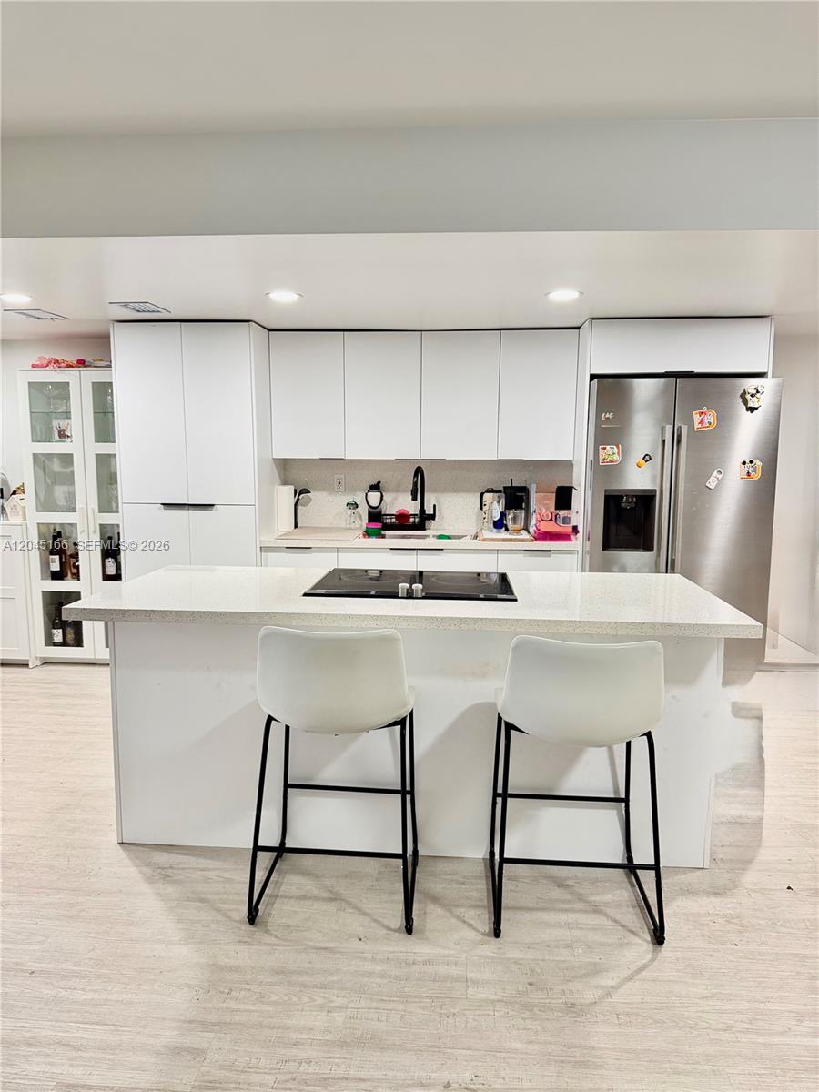 A modern kitchen features white cabinetry, a central island with a cooktop, and stainless appliances — 8010 NW 27th Pl # 8010, Sunrise FL 33322, SUNRISE, FL