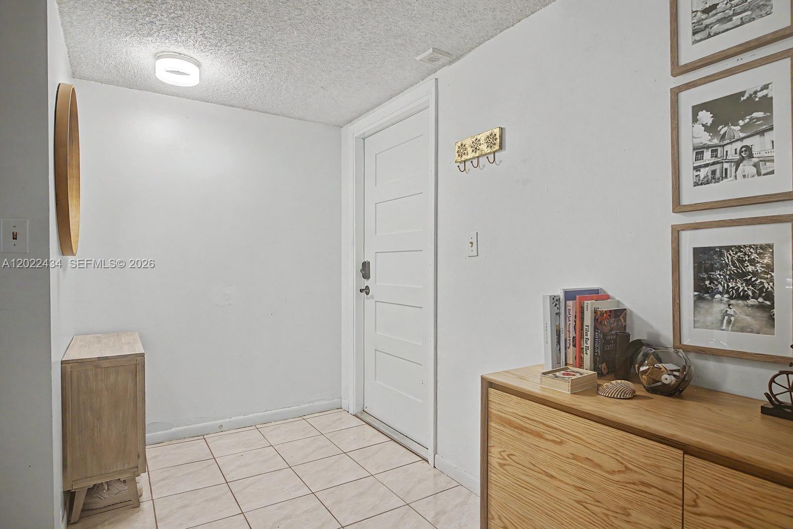 An entryway features a white door, tiled floor, wood furniture, and framed wall art — 13045 SW 68th St # 111, Miami FL 33183, MIAMI, FL