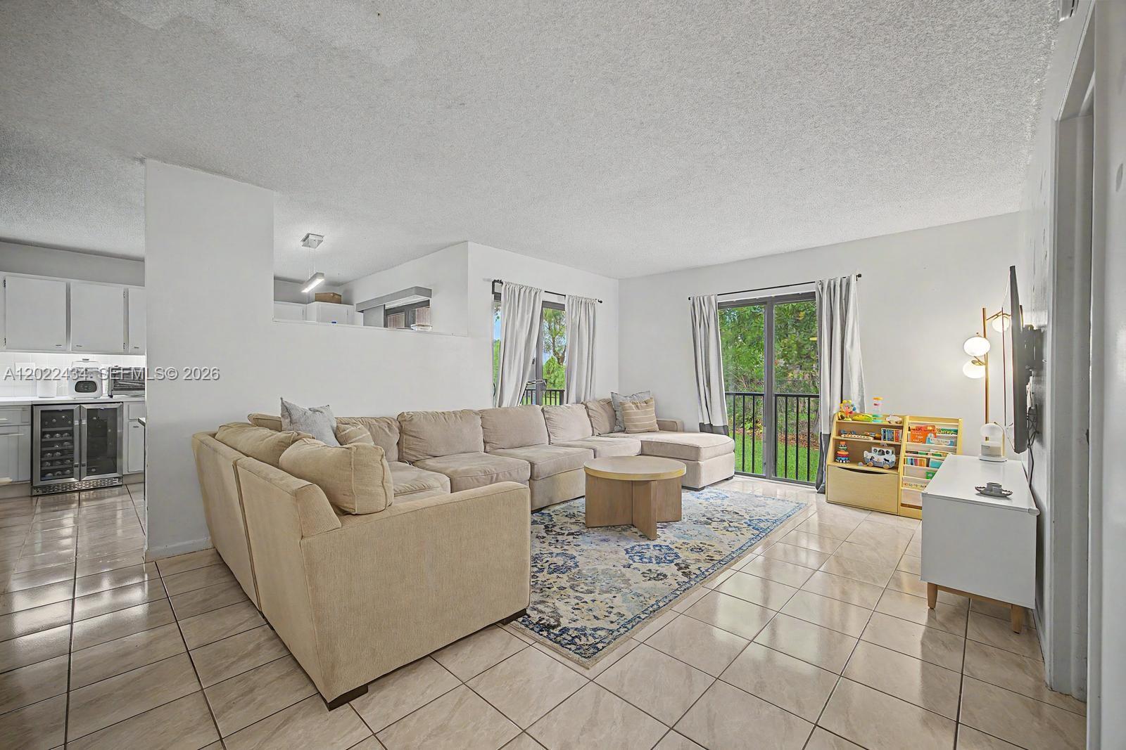 A living room features a large beige sectional sofa, a patterned rug, and tile flooring — 13045 SW 68th St # 111, Miami FL 33183, MIAMI, FL