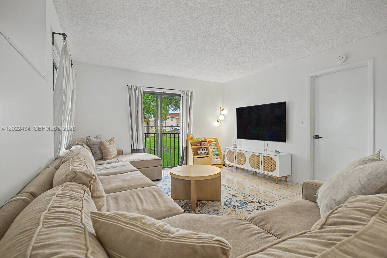 A living room features a large sectional sofa, a round coffee table, and a television — 13045 SW 68th St # 111, Miami FL 33183, MIAMI, FL