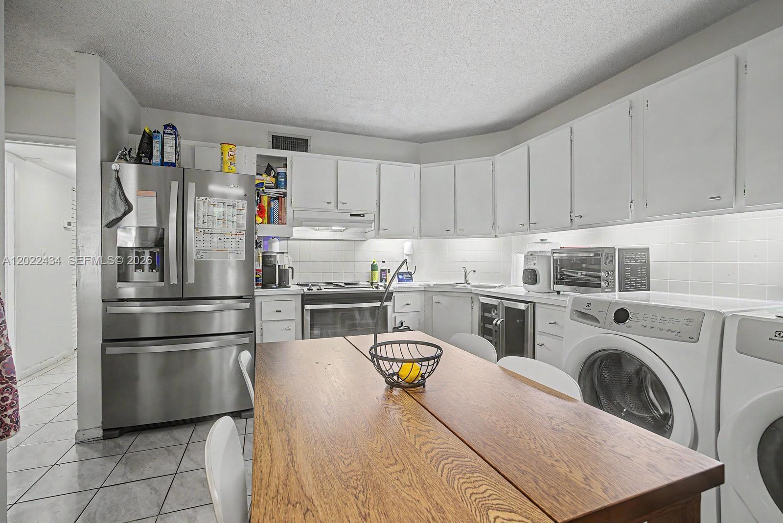 A kitchen features white cabinetry, stainless steel appliances, a wooden table, and a laundry unit — 13045 SW 68th St # 111, Miami FL 33183, MIAMI, FL