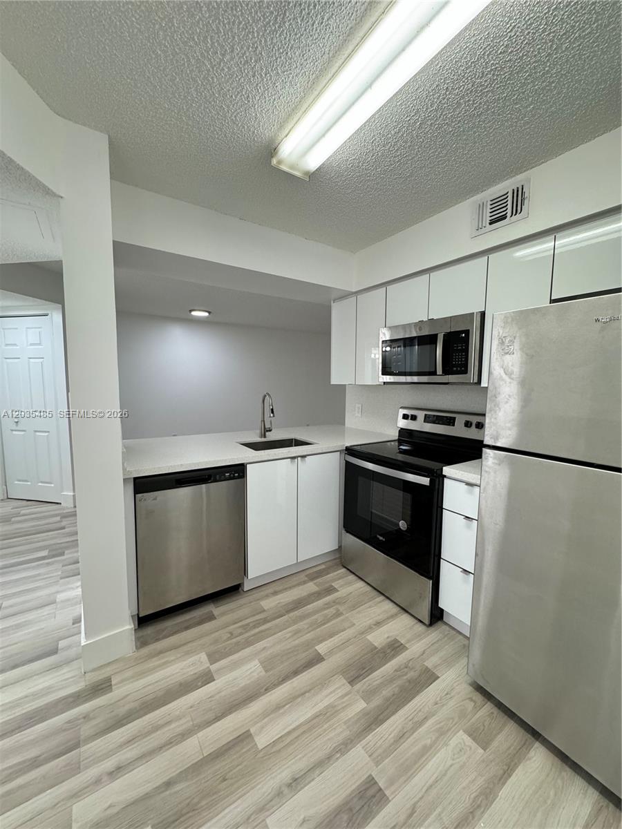 A kitchen features stainless steel appliances, white cabinetry, and light wood-look flooring — CORAL SPRINGS, FL