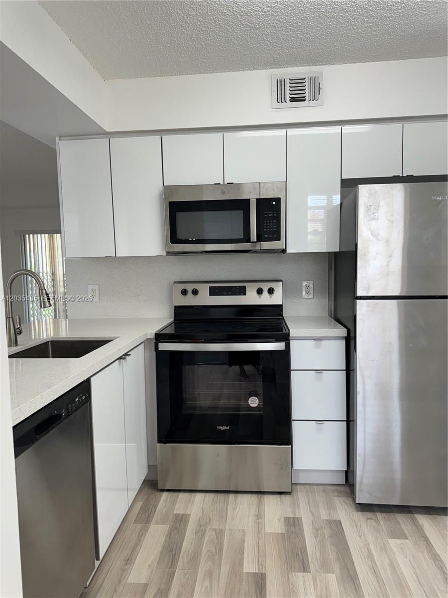 A modern kitchen features white cabinets, stainless steel appliances, and light-colored countertops — CORAL SPRINGS, FL