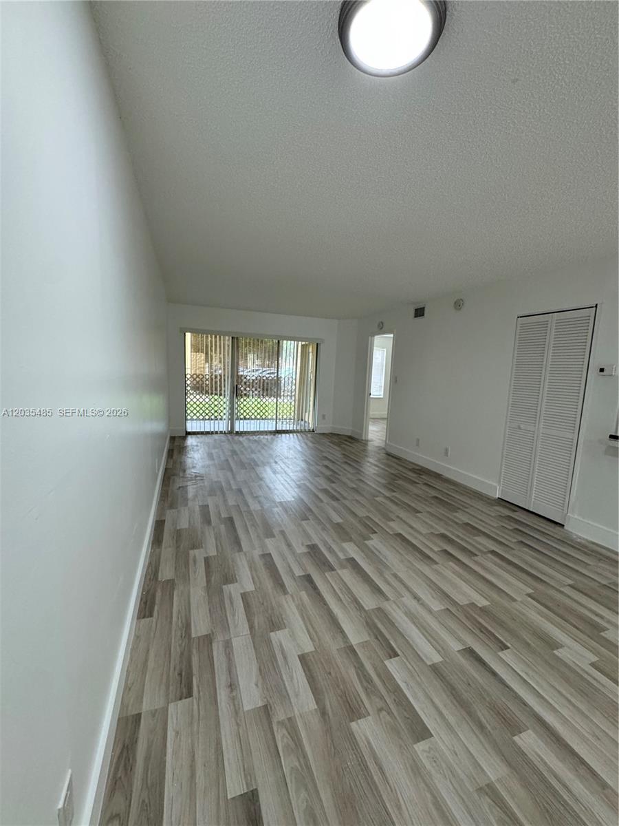 This living area features light wood-look flooring, white walls, and a sliding glass door — CORAL SPRINGS, FL