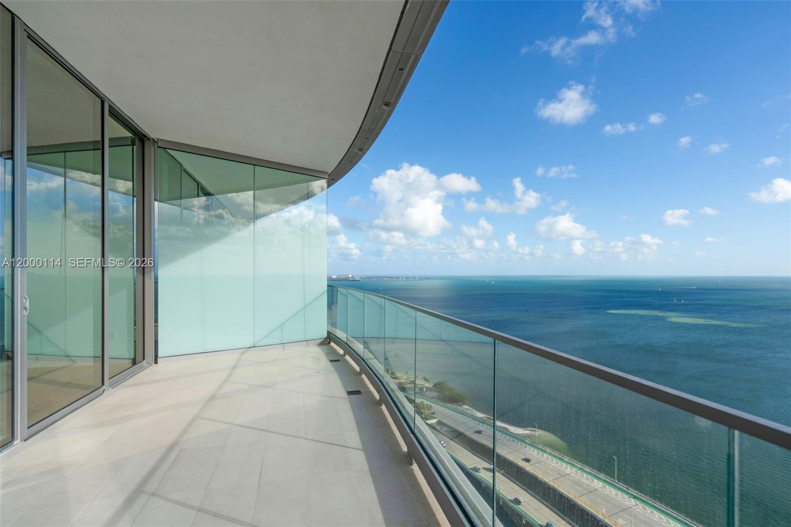 A curved balcony with glass railings overlooks the ocean and a coastal highway — 175 SE 25 RD # 3003, Miami FL 33129, MIAMI, FL