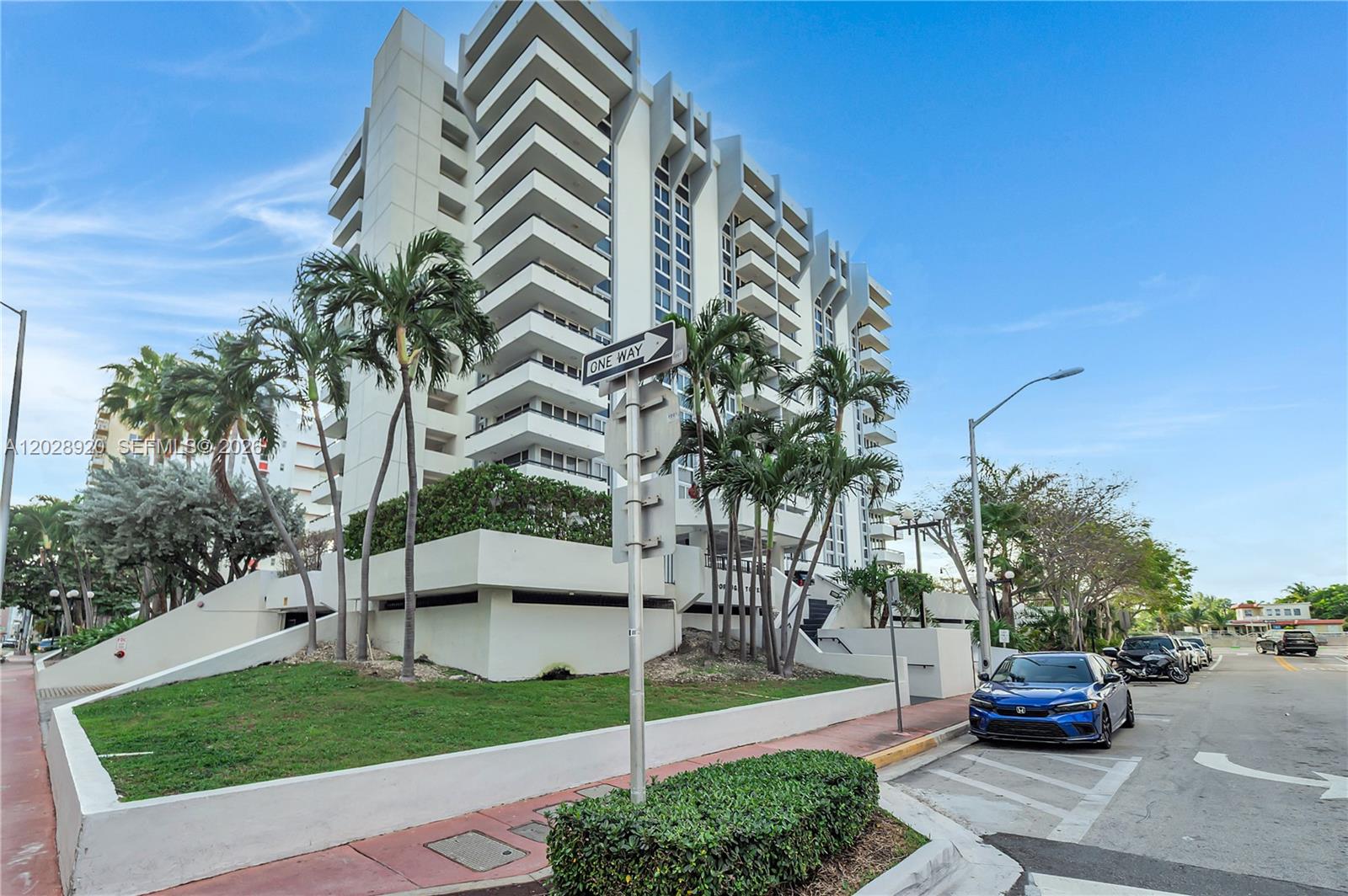 A multi-story white apartment building stands behind palm trees and a parked blue car — 3200 Collins Ave # 8, Miami Beach FL 33140, MIAMI BEACH, FL