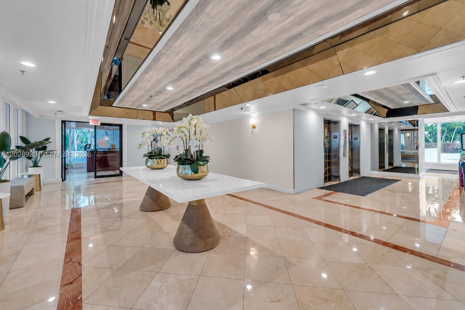 A bright lobby features a long white table, two large orchid arrangements, and mirrored ceilings — 3200 Collins Ave # 8, Miami Beach FL 33140, MIAMI BEACH, FL