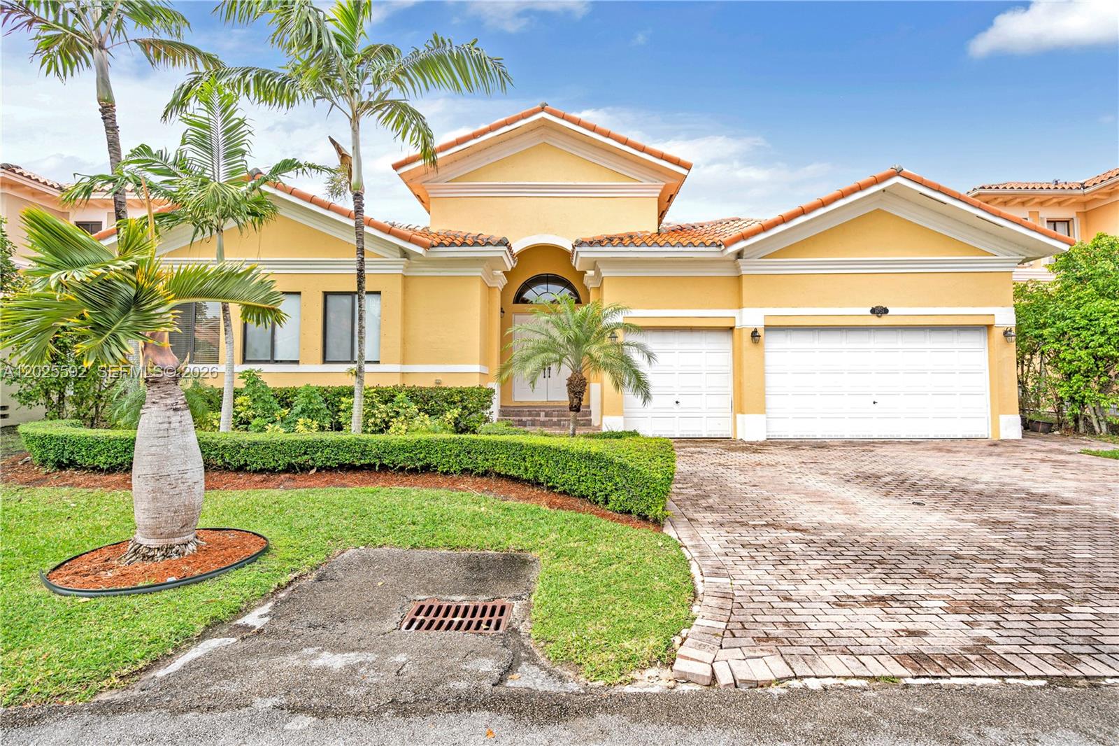 A yellow single-story house with a tile roof, two-car garage, and a brick driveway — CUTLER BAY, FL