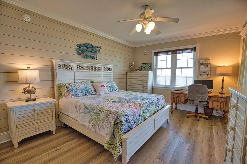 A bedroom features a white bed, shiplap accent wall, desk, and wood-look flooring — 1116 S MCCALL ROAD UNIT 121, ENGLEWOOD, FL