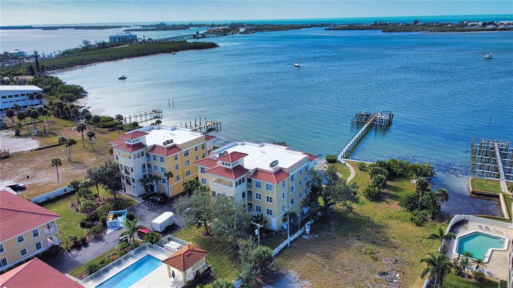 An aerial view shows waterfront apartment buildings with swimming pools and a wooden boat dock — 1116 S MCCALL ROAD UNIT 121, ENGLEWOOD, FL