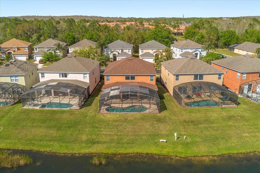 An aerial view shows three houses with screened-in pools overlooking a pond and trees — 4692 GOLDEN BEACH COURT, KISSIMMEE, FL
