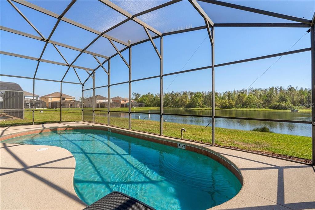 A screened-in swimming pool overlooks a lake behind a residential neighborhood — 4692 GOLDEN BEACH COURT, KISSIMMEE, FL