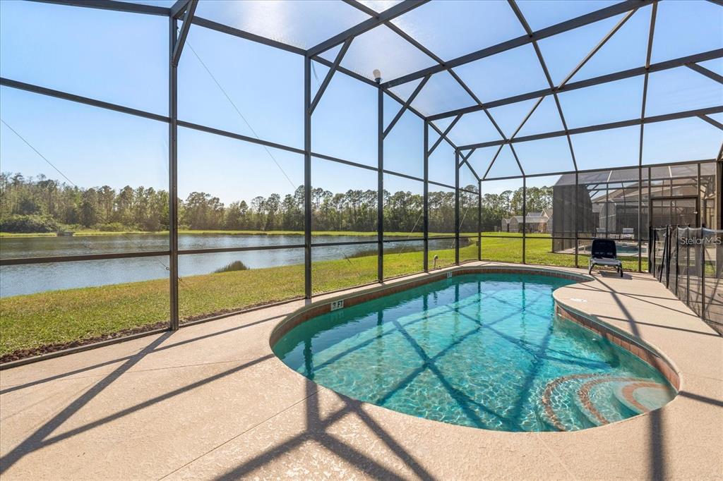 A screened-in pool patio overlooks a lake with a grassy lawn and surrounding trees — 4692 GOLDEN BEACH COURT, KISSIMMEE, FL