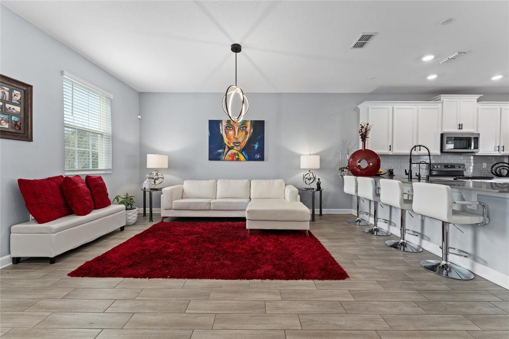 A living room and kitchen area with light gray walls, white furniture, and red accents — 14095 TITLE WAY, WINTER GARDEN, FL