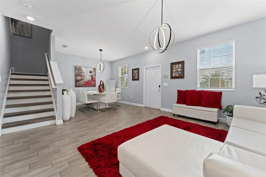 A living and dining area features light wood-look tile floors, a staircase, and red accents — 14095 TITLE WAY, WINTER GARDEN, FL