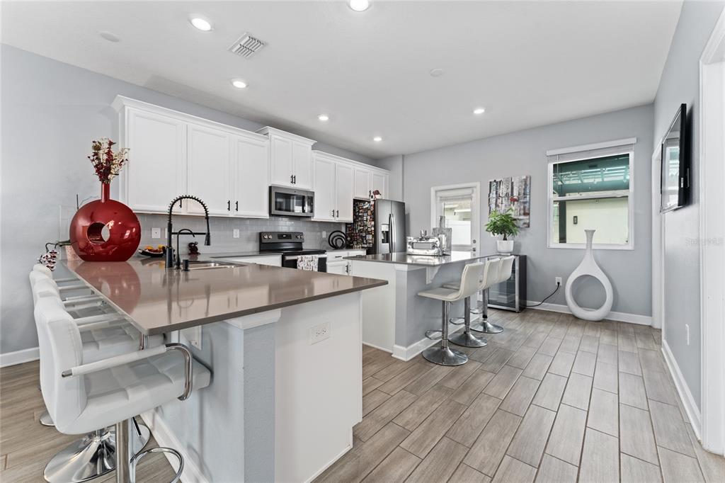 A modern kitchen features white cabinets, a large island with bar seating, and tile flooring — 14095 TITLE WAY, WINTER GARDEN, FL