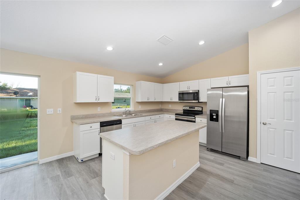 A kitchen with white cabinets, stainless steel appliances, a center island, and light wood flooring — 14162 SW 16TH PLACE, DUNNELLON, FL