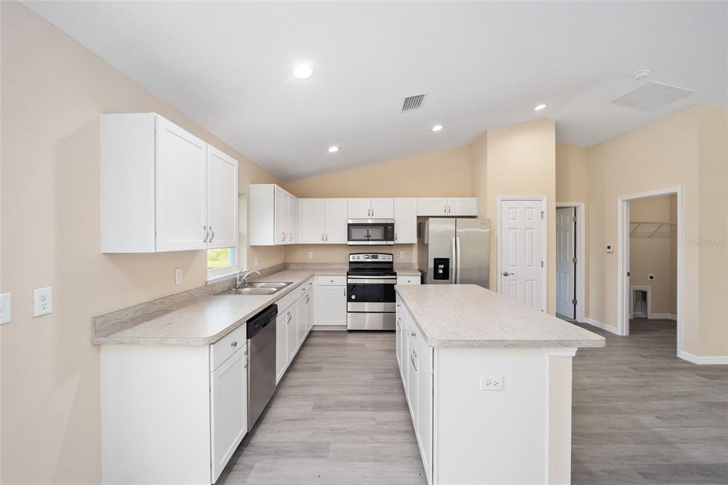 A kitchen with white cabinets, stainless steel appliances, a center island, and wood-look flooring — 14162 SW 16TH PLACE, DUNNELLON, FL