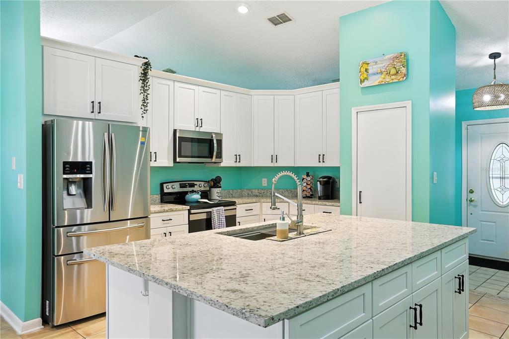 A kitchen features white cabinetry, a granite-topped island, stainless steel appliances, and turquoise walls — 818 WIL O WIK DRIVE, CASSELBERRY, FL