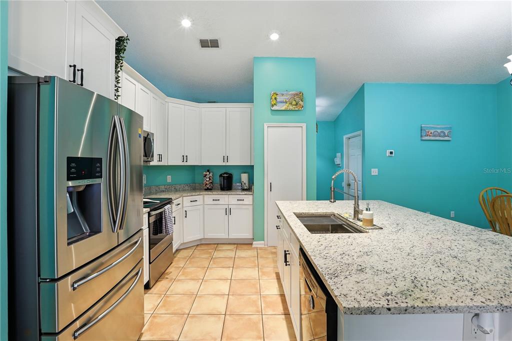 A kitchen features white cabinets, granite countertops, stainless steel appliances, and bright turquoise walls — 818 WIL O WIK DRIVE, CASSELBERRY, FL