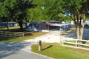 A single-story house with a screened porch and carport sits behind a wooden fence — 8047 CINDY DRIVE, ZEPHYRHILLS, FL